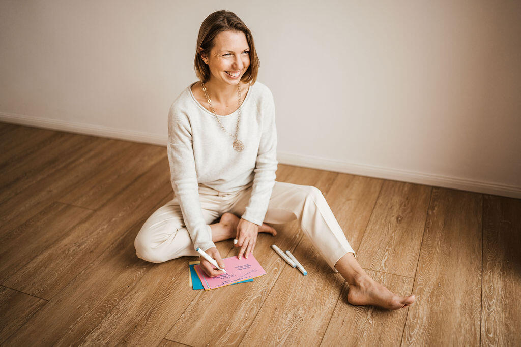 Fiona schreibt sitzend am Boden mit farbigen Coaching Karten und Stiften